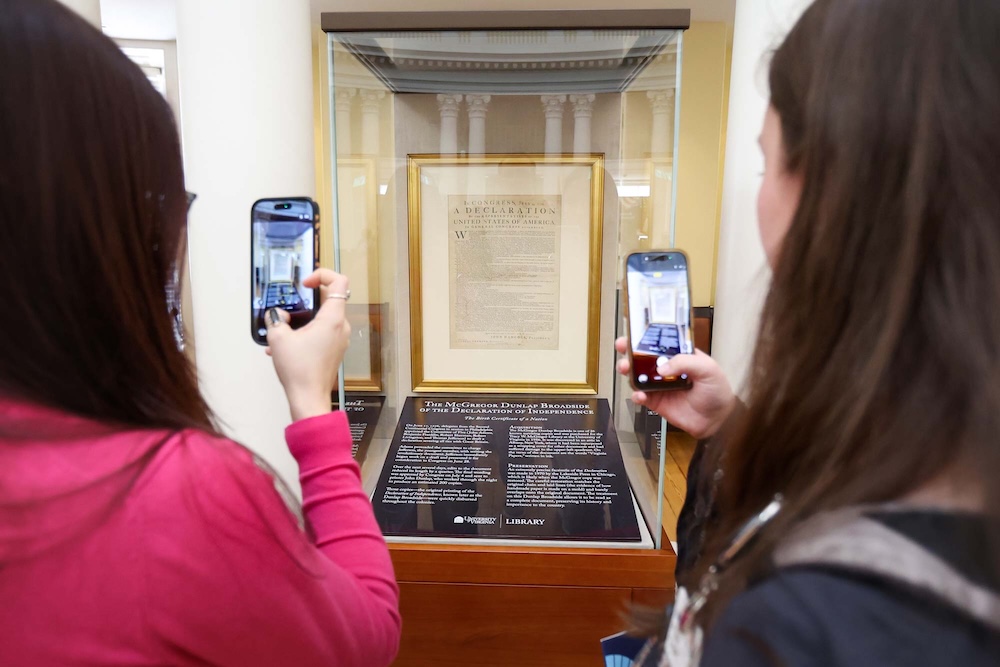 Two individuals are photographing a display case containing an original document of The Declaration of Independence in the Rotunda.