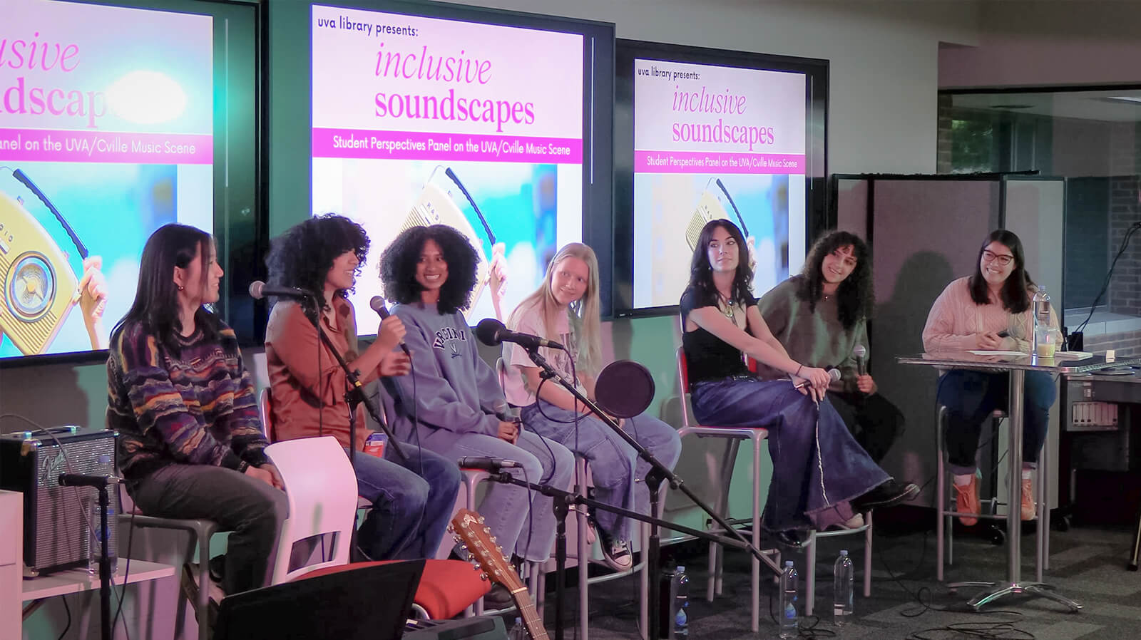 Seven individuals seated on stage participating in a panel discussion titled "Inclusive Soundscapes" at a live library event. Three large screens in the background display the event name.