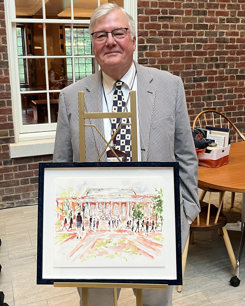 Man in a suit, tie, and glasses, standing behind an easel holding a painting of the exterior of a large building.