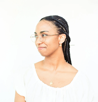 A photograph of a young woman in semi-profile, wearing glasses and smiling
