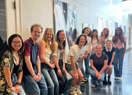 A group of students poses in front of a long hallway featuring tall printouts hung on the walls